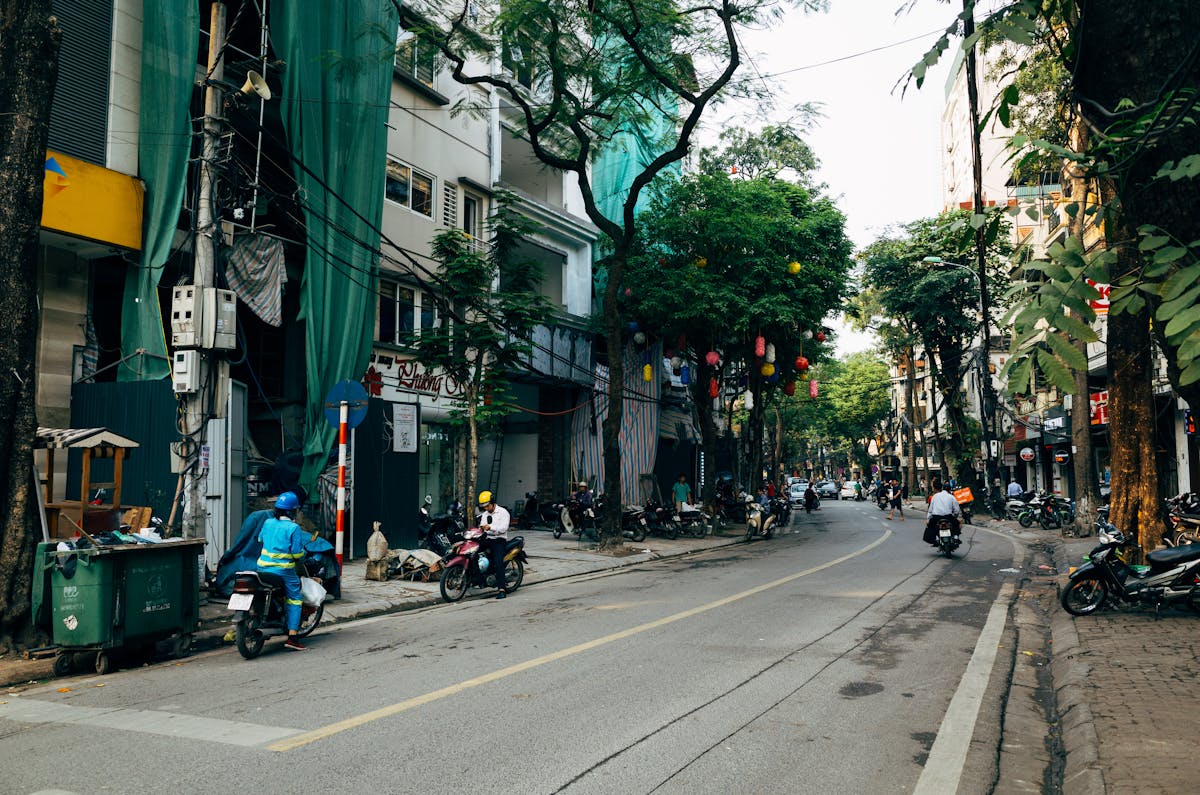 Busy Hanoi street scene with motorbikes and trees showing typical Vietnam traffic