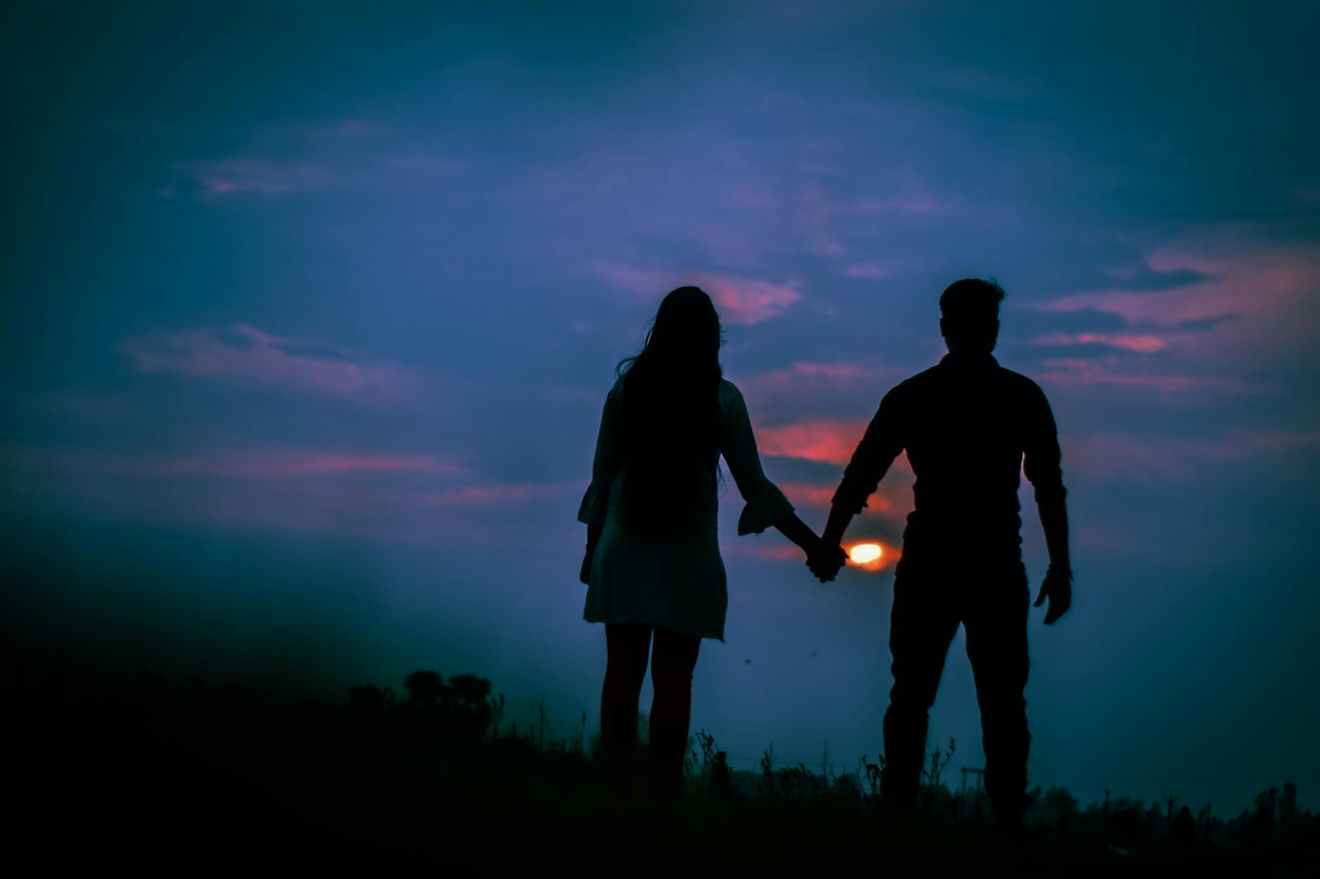 Silhouetted couple holding hands against vibrant sunset