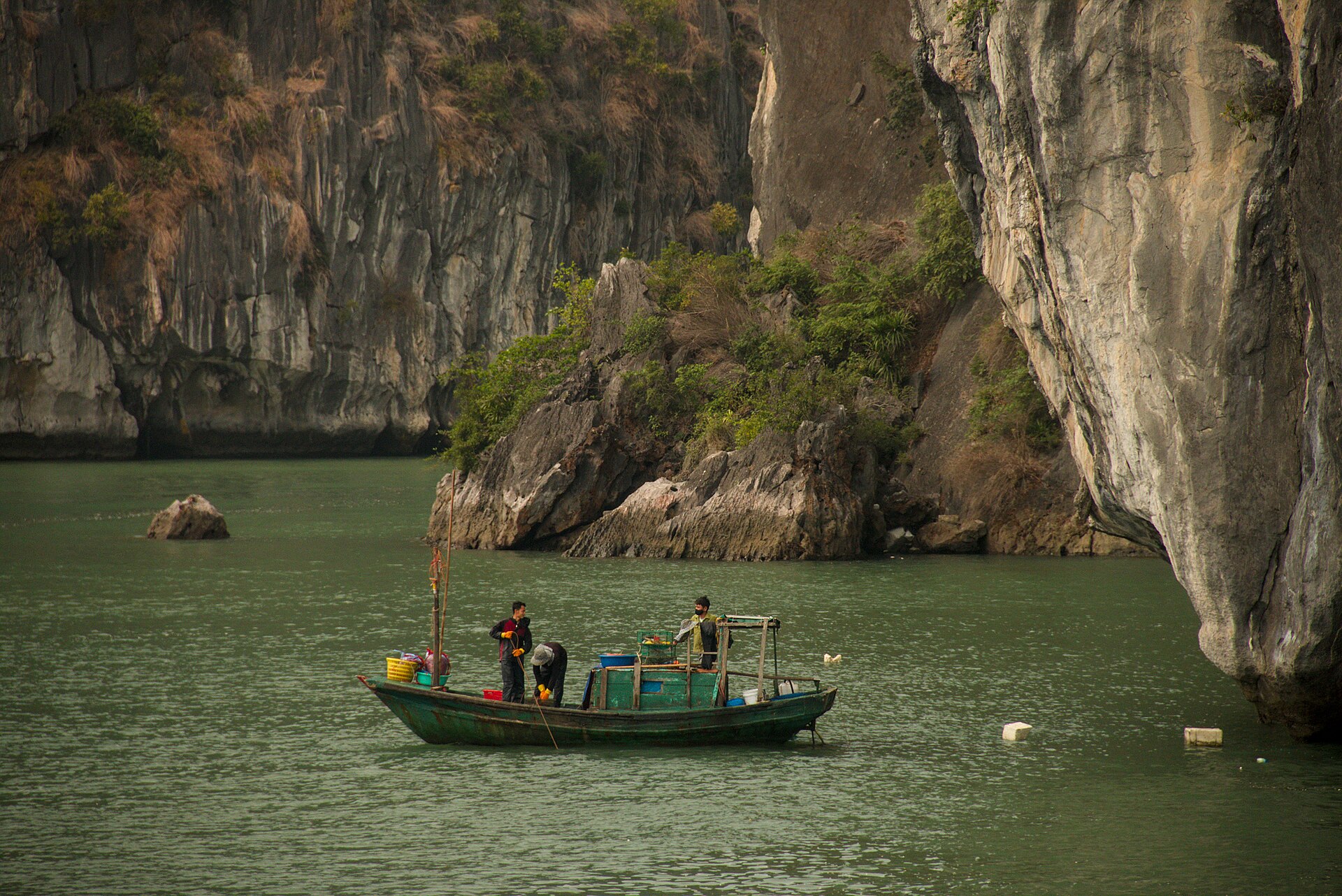 Bai Tu Long Bay: The Quiet Third Option 2 Three fishermen working from a green wooden boat below sheer limestone cliffs