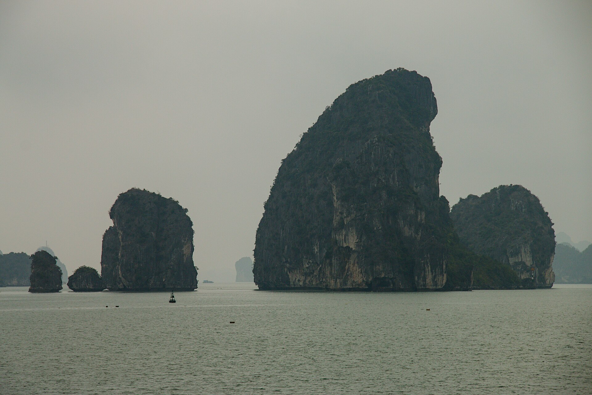 Bai Tu Long Bay: The Quiet Third Option 1 Tall limestone islands rising from grey, misty water in Bai Tu Long Bay, with a navigation buoy in the foreground
