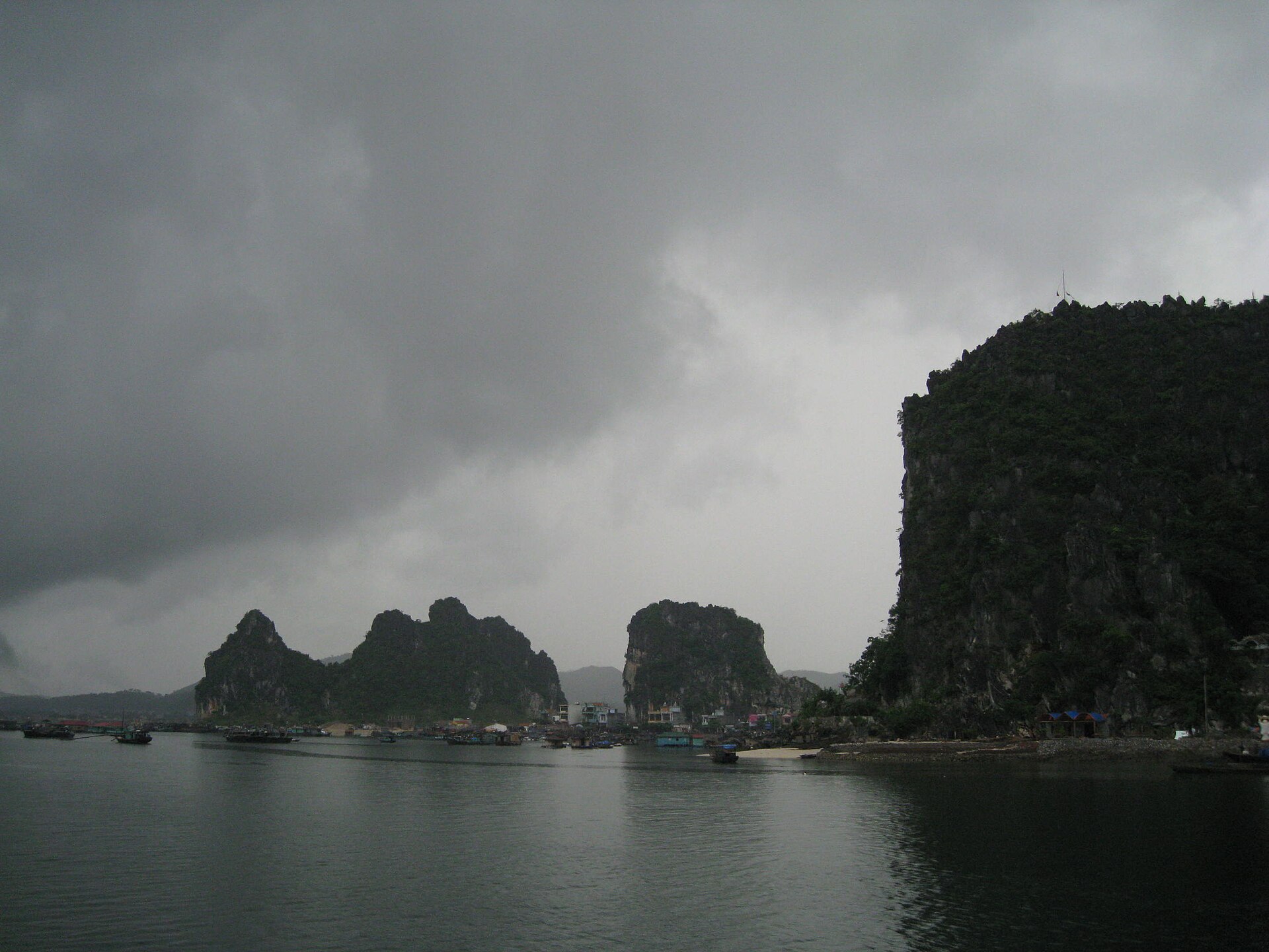 Bai Tu Long Bay: The Quiet Third Option 3 A small island fishing settlement at the foot of limestone cliffs under heavy storm clouds in Bai Tu Long Bay