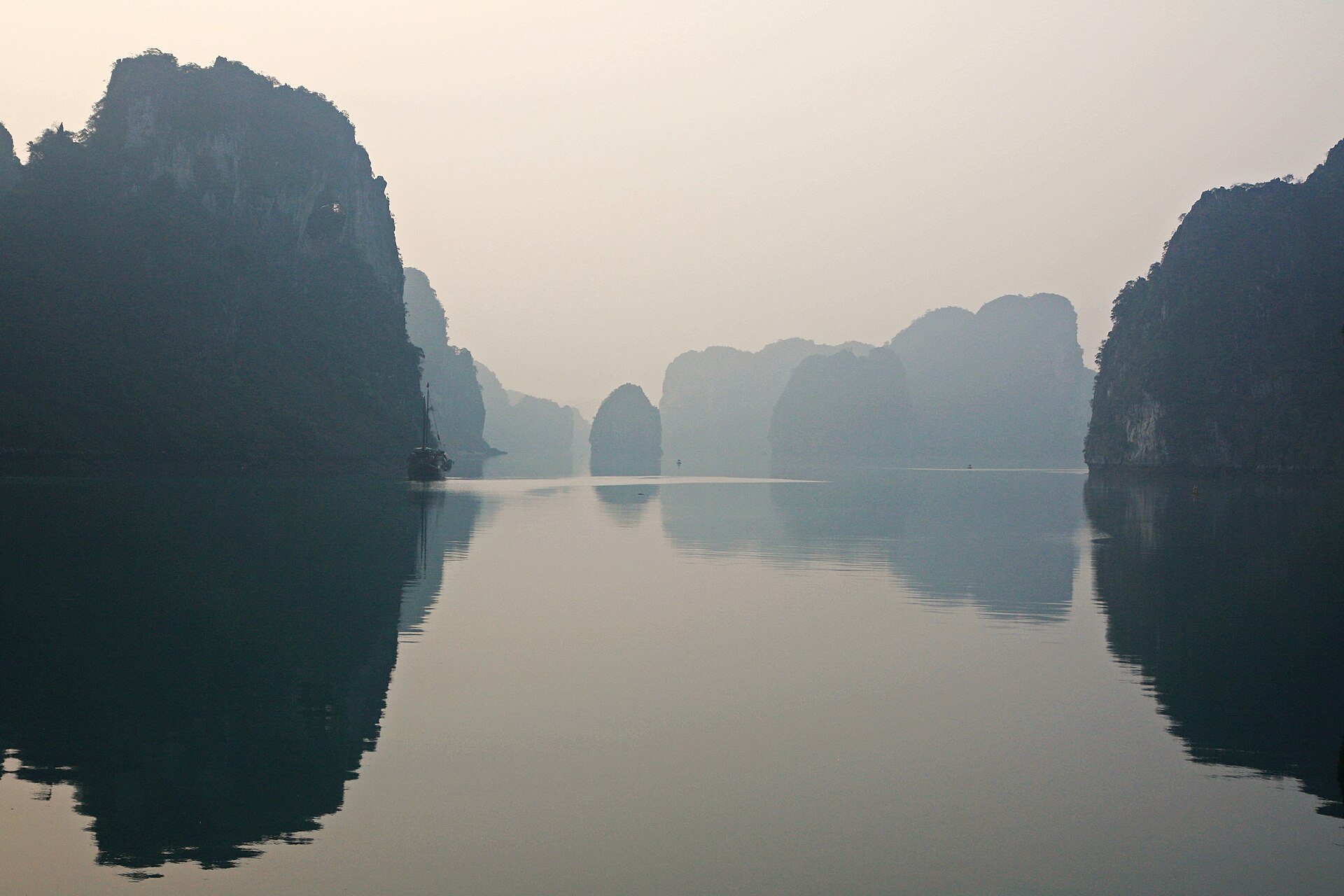 Ha Long Bay 2 Day 1 Night: What the Itinerary Actually Looks Like 3 Mist over perfectly still water between steep limestone islands at dawn, with a single junk at anchor
