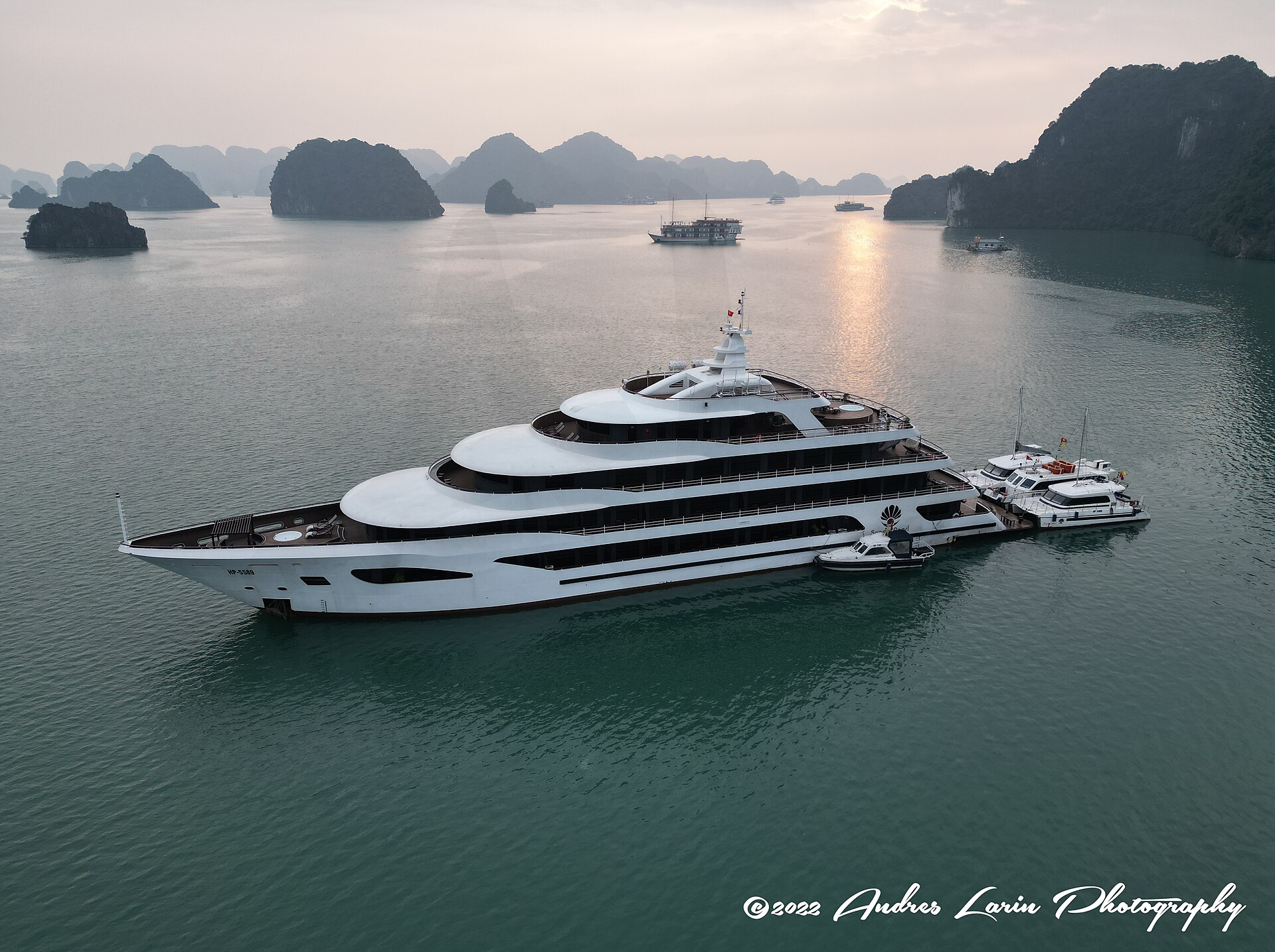 Best Ha Long Bay Cruises: How to Choose (Not a Top 10) 3 A large modern white cruise ship anchored among misty limestone islands with several tenders tied alongside