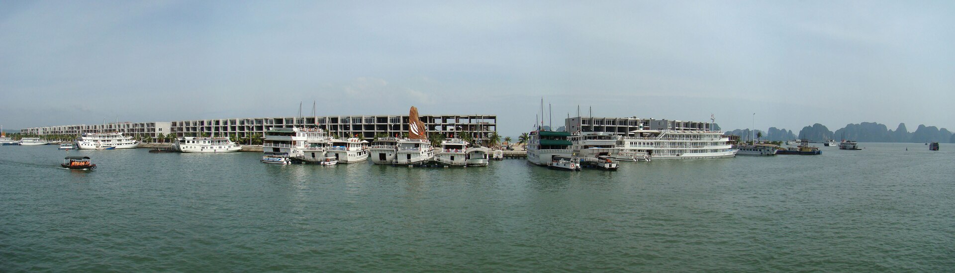 Best Ha Long Bay Cruises: How to Choose (Not a Top 10) 4 A long row of white cruise boats moored at a harbour in Ha Long, with limestone islands on the horizon