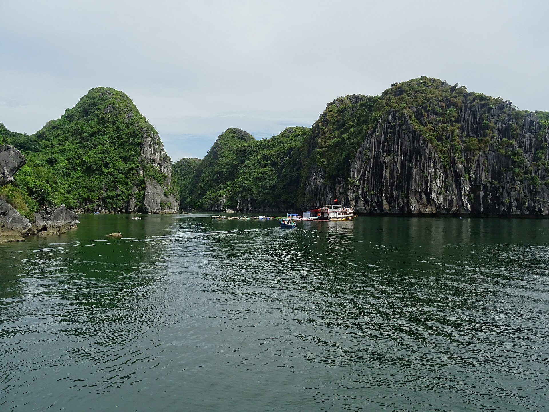 Lan Ha Bay vs Ha Long Bay: Which to Book 4 A small boat heading towards a floating fish farm at the entrance to a lagoon ringed by limestone cliffs in Lan Ha Bay