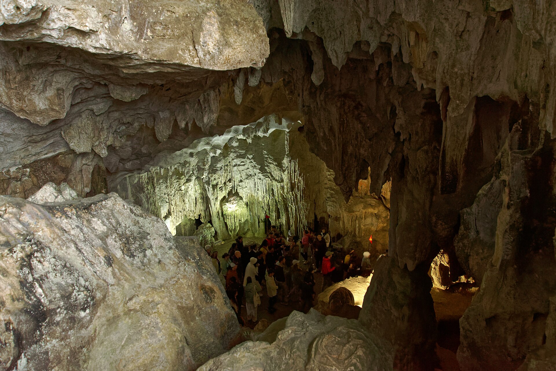 A tour group walking through the lit main chamber of Sung Sot Cave among stalactites